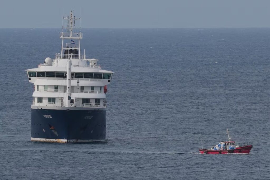 Barco MV Hondius navegando en el océano con un bote pequeño cerca.