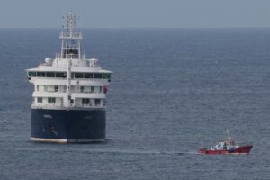 Barco MV Hondius navegando en el océano con un bote pequeño cerca.
