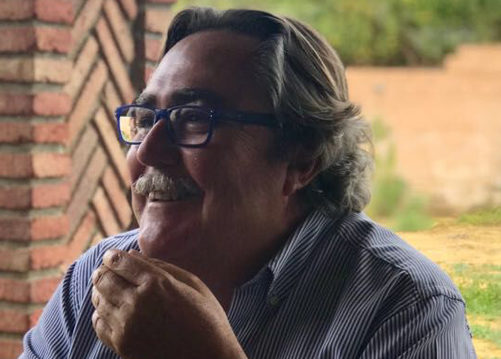 Hombre sonriendo en un entorno informal, con fondo natural.