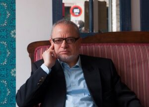 Retrato de Ramiro Grau sentado en un sofá con fondo decorativo