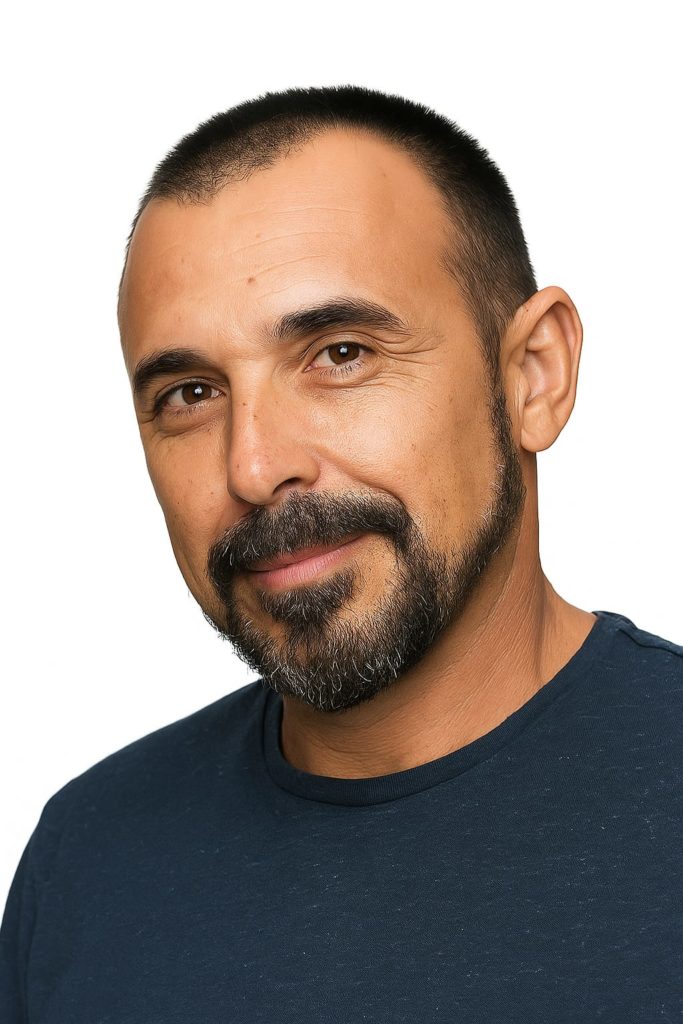 Retrato de un hombre con barba y camiseta oscura sonriendo.