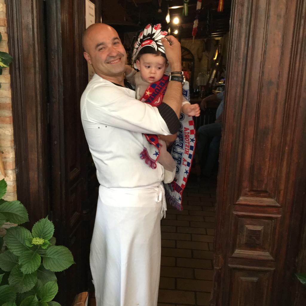 Niño vestido de indio con camiseta del Atlético de Madrid en brazos de su padre.