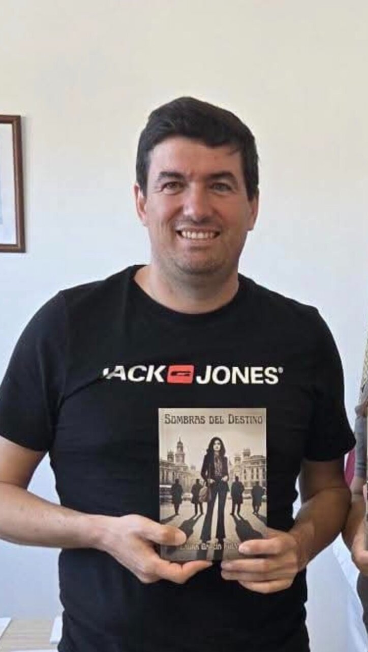 Hombre sosteniendo un libro titulado Sombras del Destino