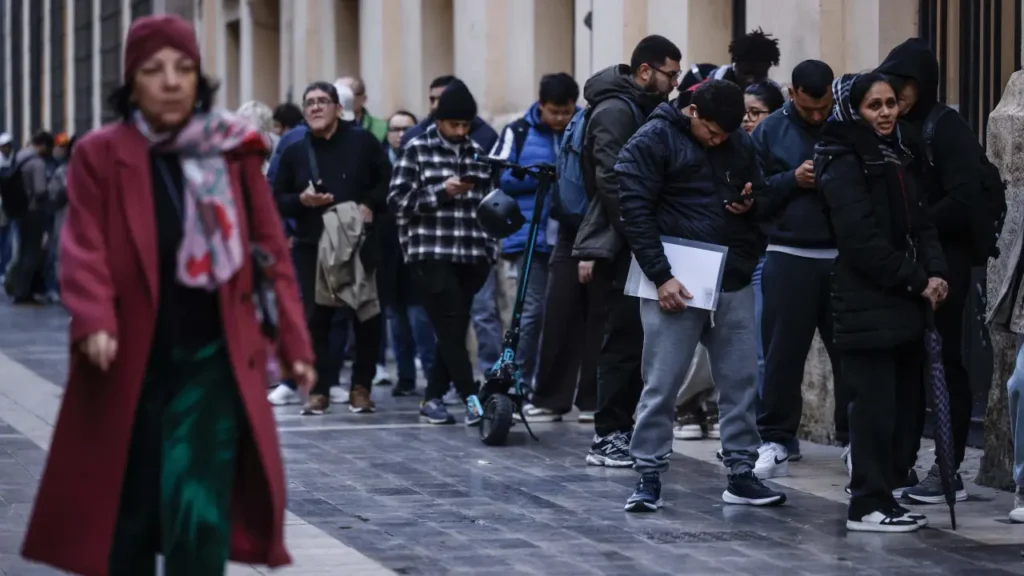 Grupo de personas en una fila en la calle, reflejando diversidad cultural.