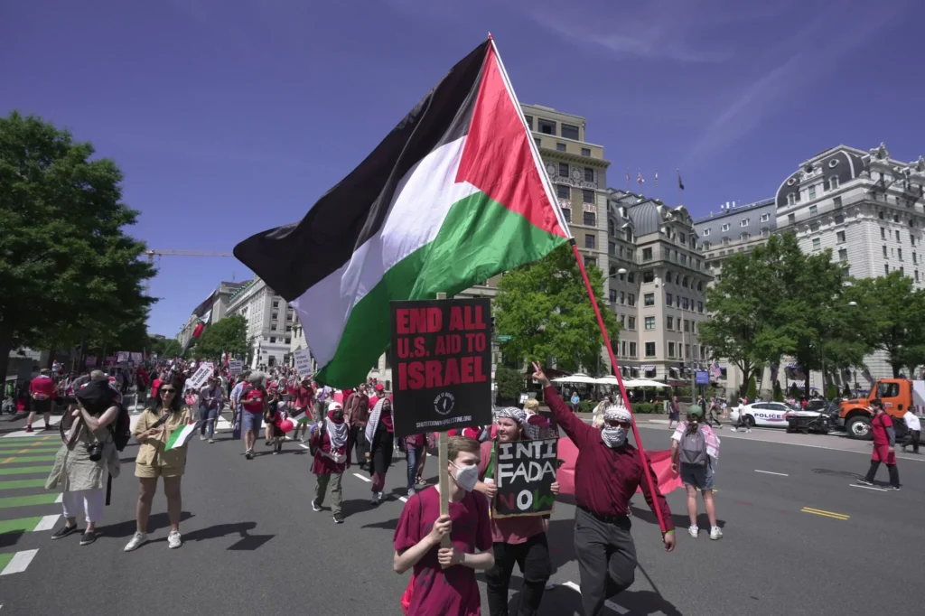 Manifestantes sosteniendo pancartas y una bandera palestina en una protesta.