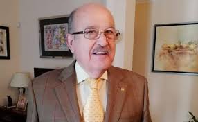 Retrato de un hombre mayor con gafas y traje en un entorno doméstico